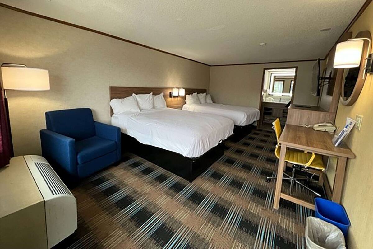 A hotel room with two beds, a desk with a chair, a lamp, and a trash bin.