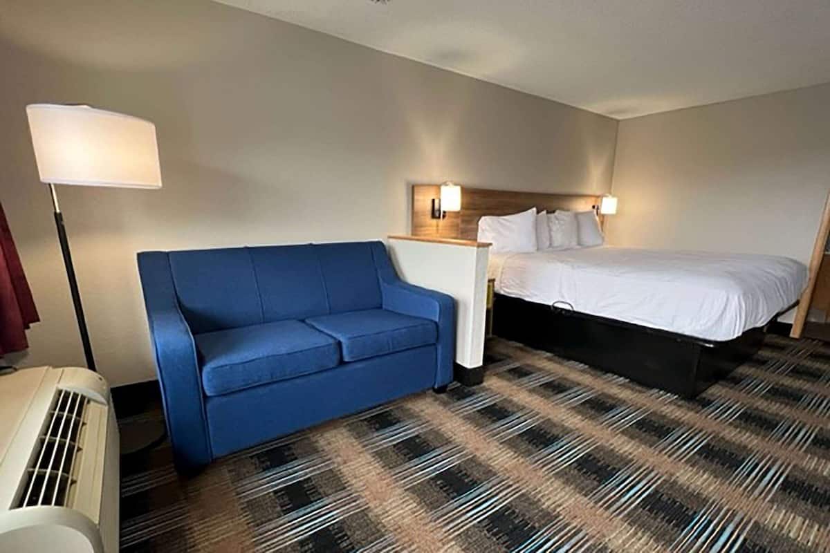 A hotel room with a blue sofa, a bed with white bedding, a lamp, and a carpeted floor.