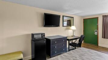 A hotel room with a bed, a desk with a chair, a television, a microwave, a dresser, and a green door.