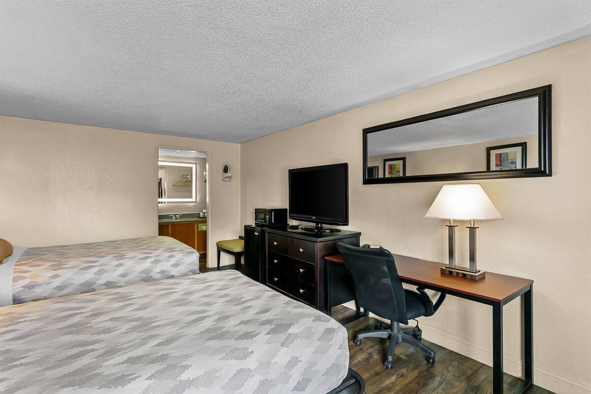 Habitación de hotel con dos camas, un escritorio con computadora y televisión, una lámpara y un espejo en la pared.