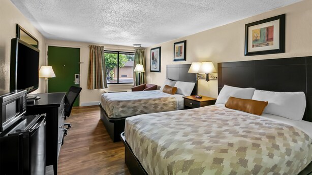 Une chambre d’hôtel avec deux lits, un bureau, une télévision et une fenêtre avec des rideaux.