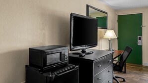 Une chambre d’hôtel avec un bureau, un téléviseur noir, un four à micro-ondes, une lampe et une porte verte.