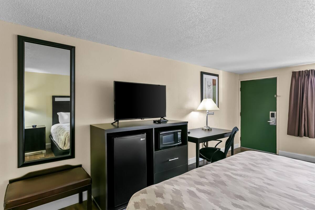 Habitación de hotel con cama, escritorio con computadora, televisión, microondas y refrigerador pequeño.