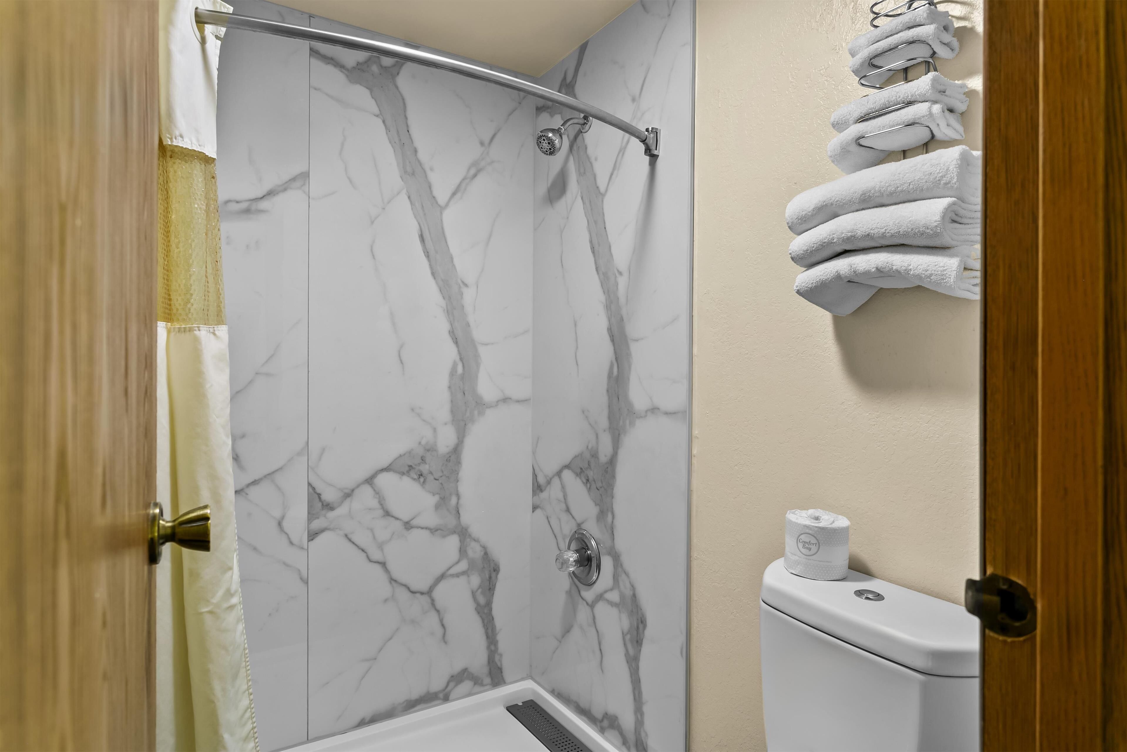 A bathroom with a shower enclosure, marble walls, a toilet, and a towel rack.