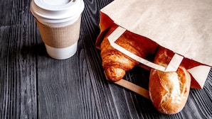 A coffee cup and a paper bag with bread on a wooden surface.