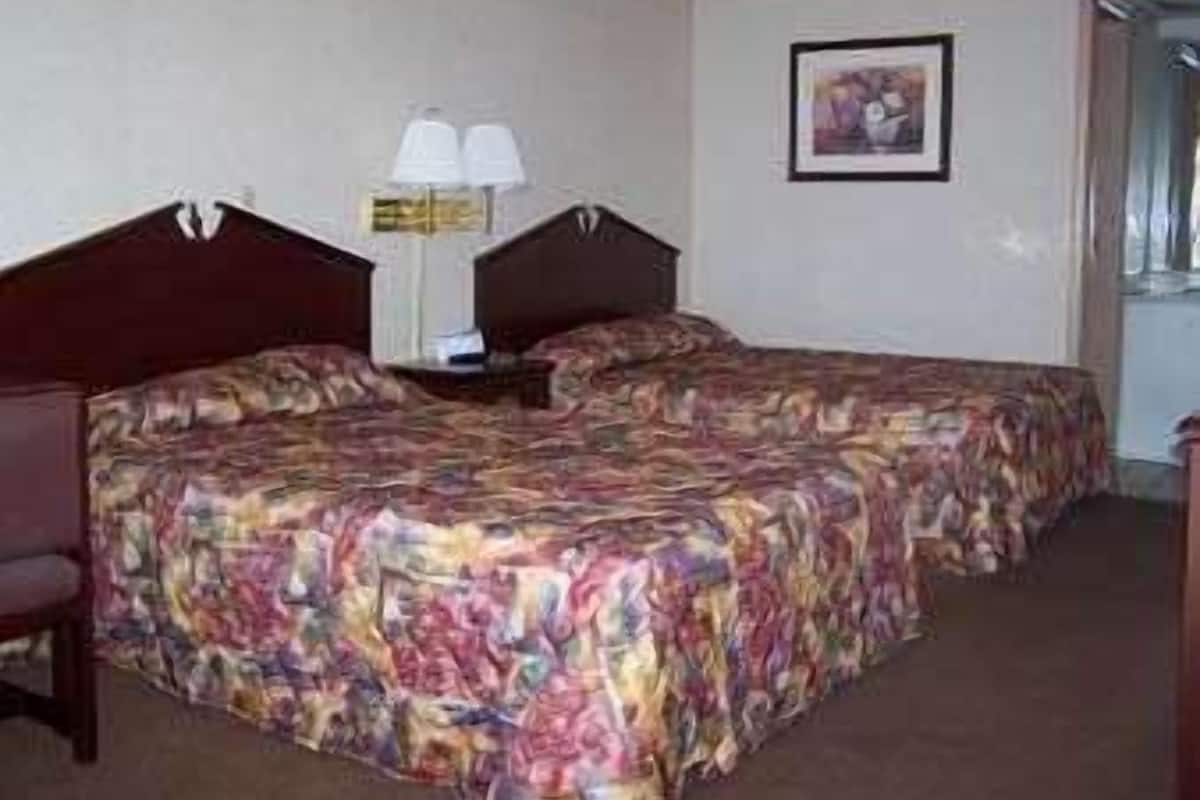 A hotel room with two beds, a nightstand, a lamp, and a framed picture on the wall.