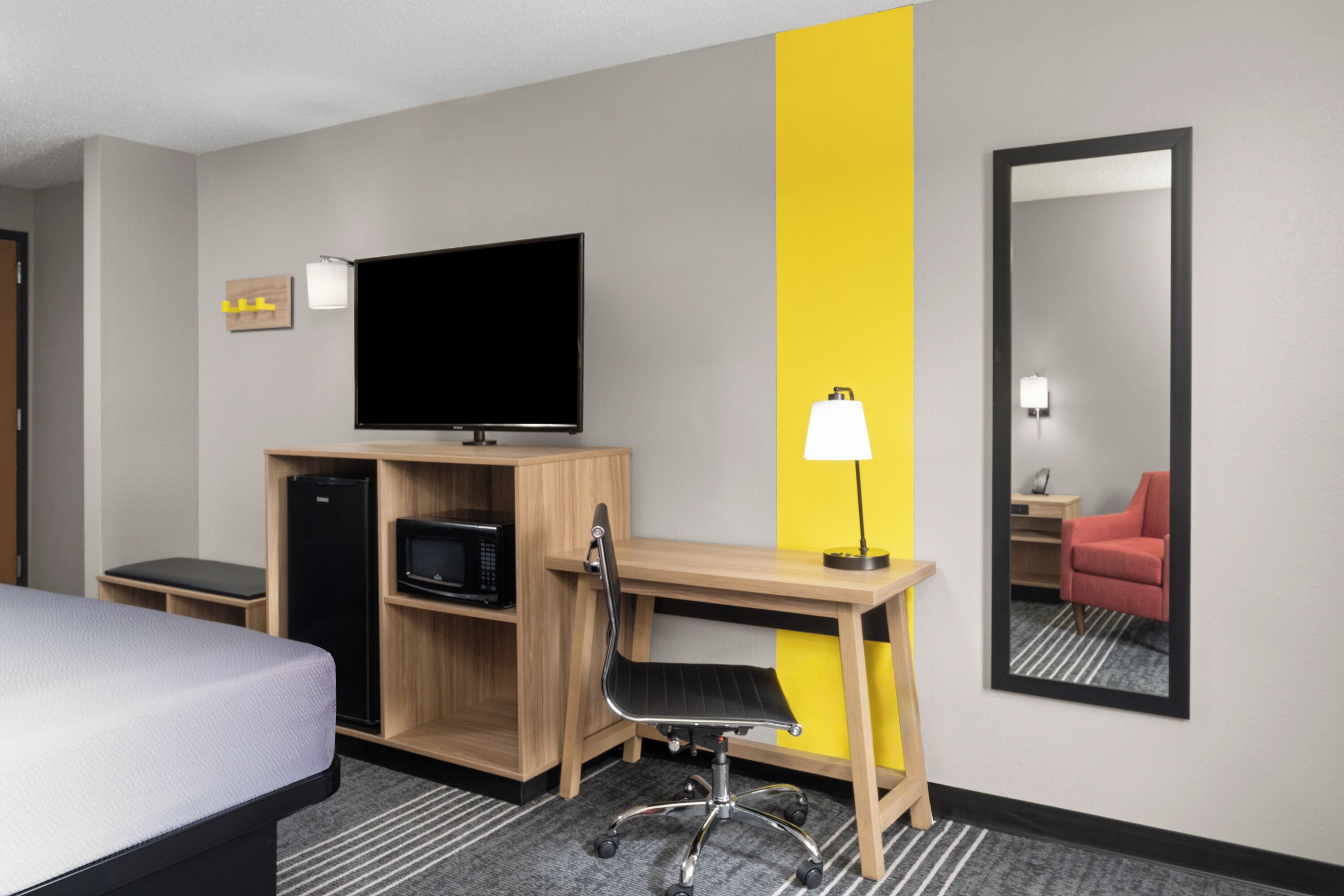 Une chambre d’hôtel équipée d’un lit, d’un bureau avec un ordinateur, d’une télévision, d’un four à micro-ondes et d’un miroir.