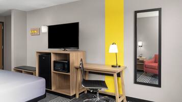 Une chambre d’hôtel équipée d’un lit, d’un bureau avec un ordinateur, d’une télévision, d’un four à micro-ondes et d’un miroir.