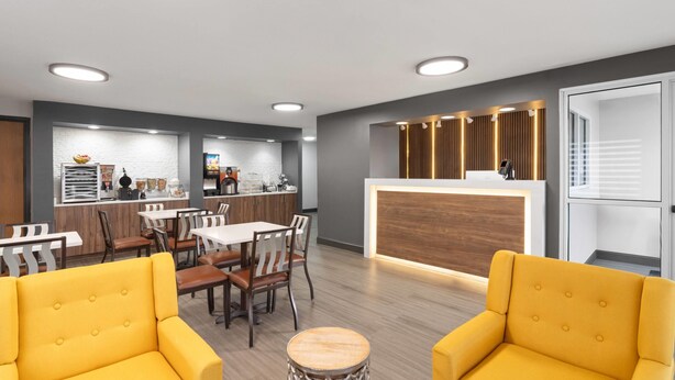 A modern hotel lobby with a reception desk, dining area, and yellow armchairs. - Super 8 by Wyndham Chattanooga East/Hamilton Place (Chattanooga)