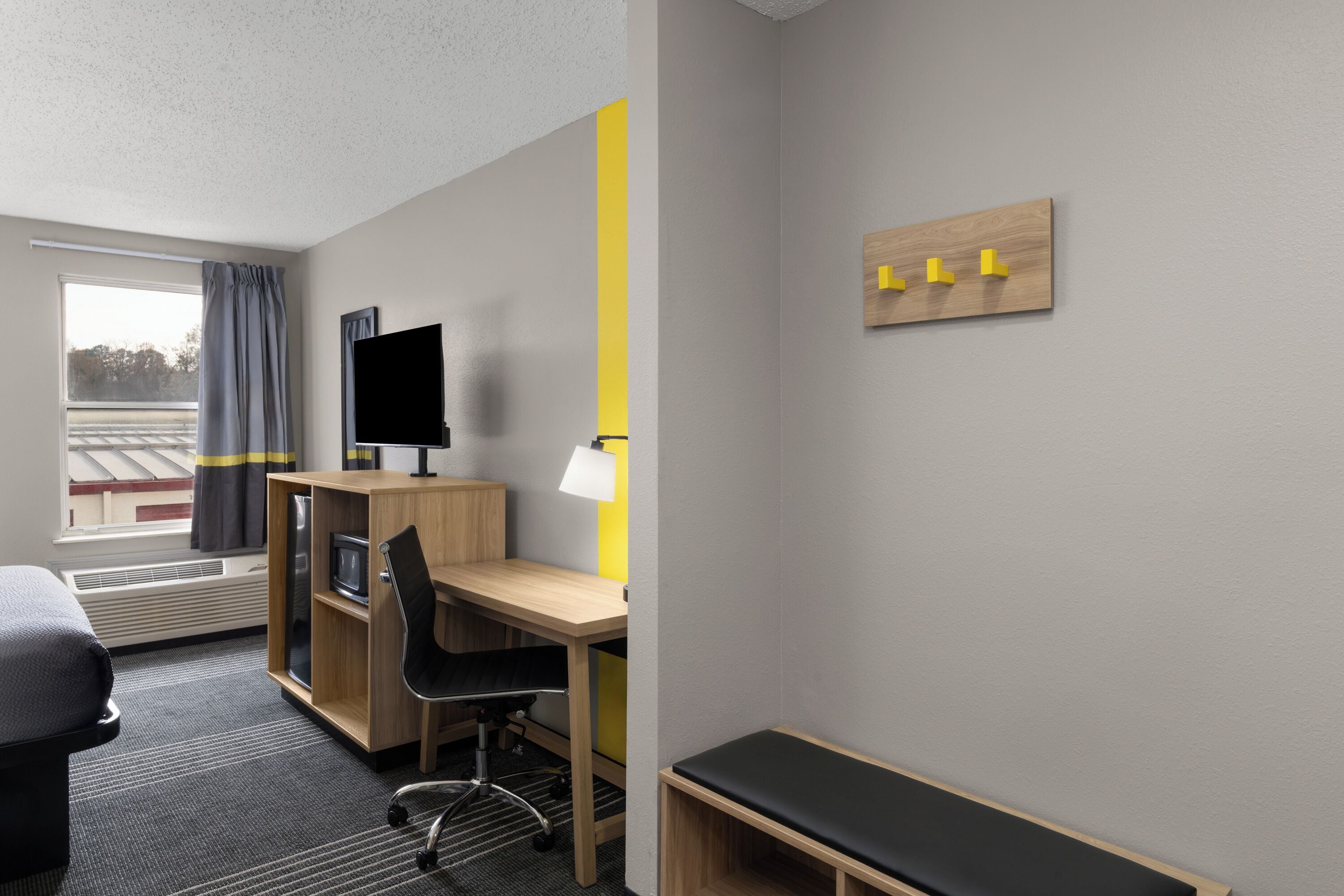 A hotel room with a desk, chair, TV, and a bed.