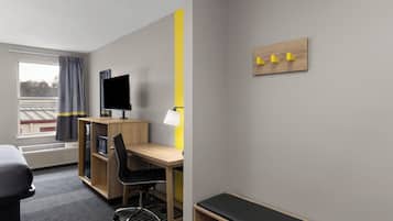 A hotel room with a desk, chair, TV, and a bed.