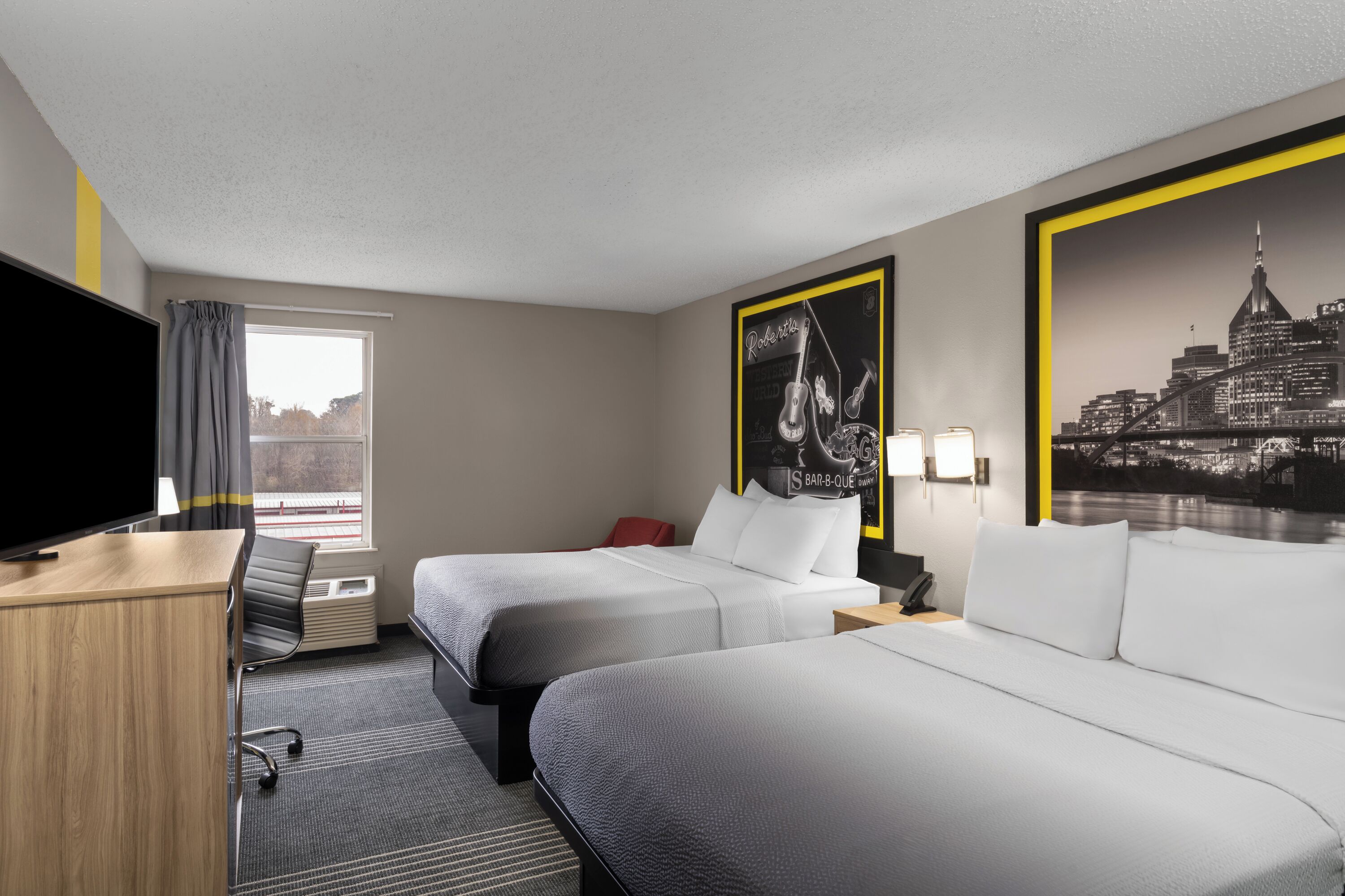 Habitación de hotel con dos camas, un escritorio, un televisor y una ventana con cortinas.