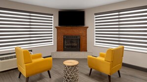 A room with two yellow chairs, a round wooden table, a fireplace, and a flat-screen TV mounted above it. - Super 8 by Wyndham Chattanooga East/Hamilton Place (Chattanooga)