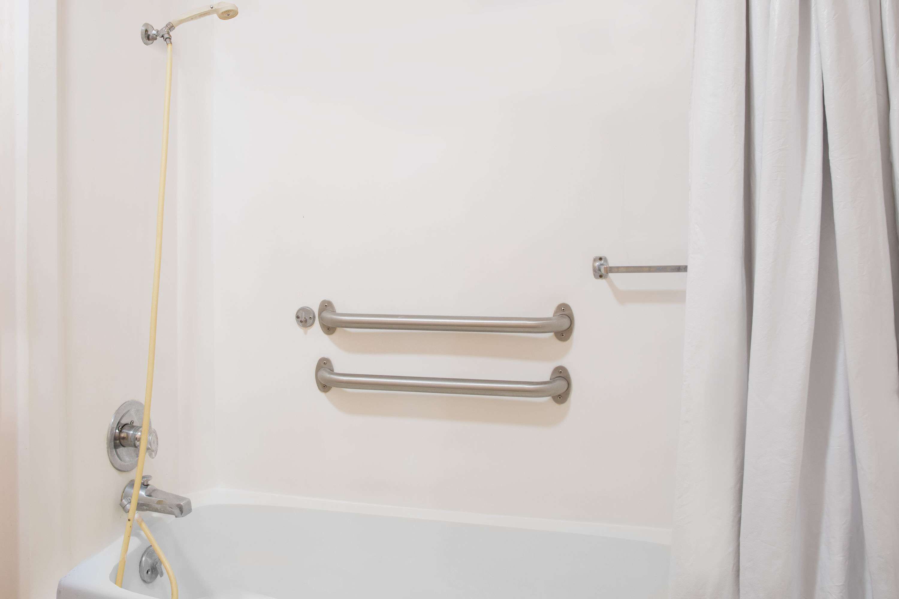 A bathroom with a bathtub, two grab bars, and a shower curtain.