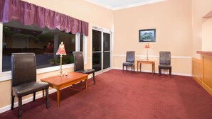 A room with a red carpet, two chairs, a small table, a lamp, a window with a purple valance, and a framed picture on the wall. - Knights Inn Augusta at Boy Scout Rd (Augusta)