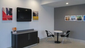 A modern waiting area with a flat-screen TV, a small table with two chairs, and a cabinet with a sign about room rates. - Motel 6 Chilhowie, VA  I-81 (Chilhowie)