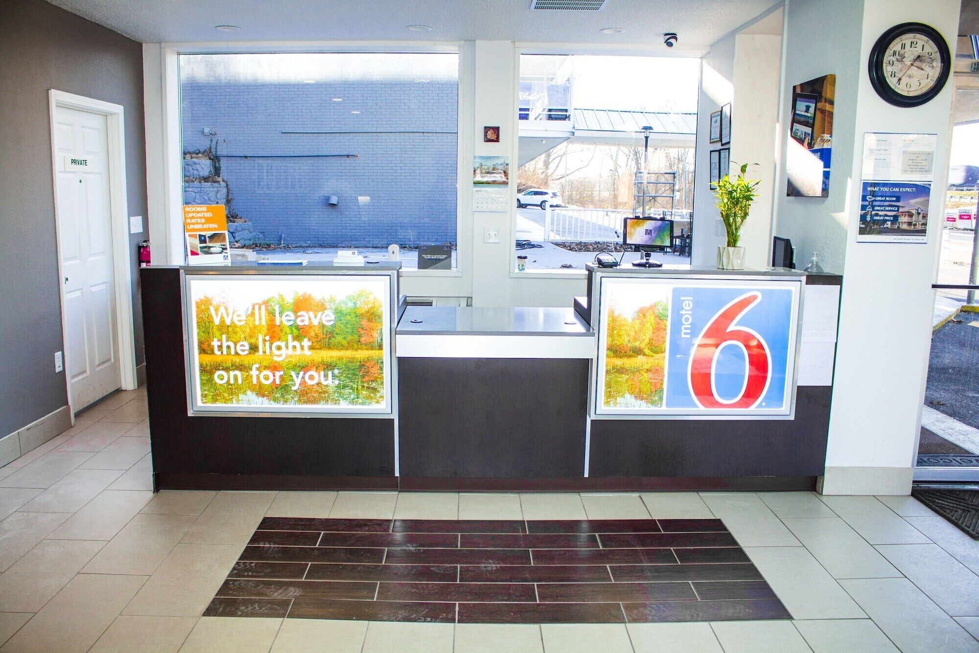 A hotel reception desk with a large sign reading "motel 6" and a message on the left saying "We'll leave the light on for you."
