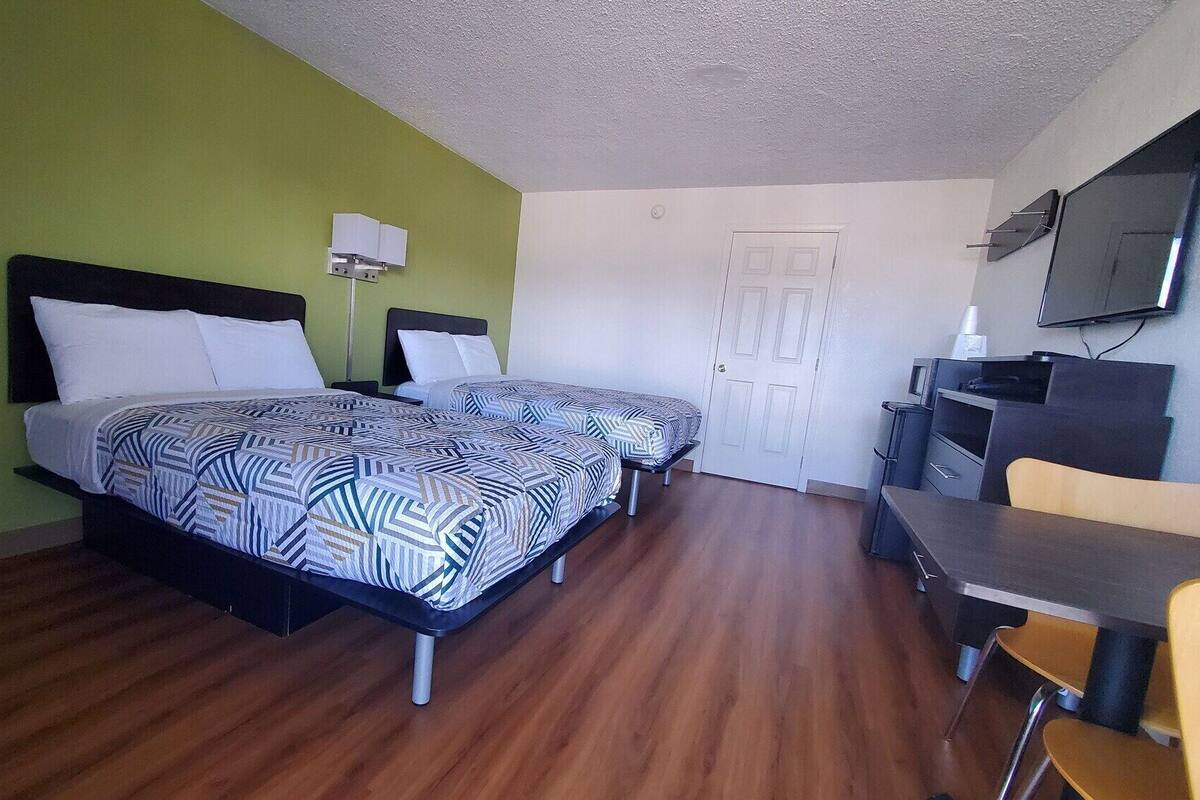 Une chambre d’hôtel avec deux lits, un bureau, une chaise, une télévision et une porte.