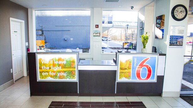A hotel reception desk with a large window, a clock on the wall, and a sign advertising the hotel. - Motel 6 Chilhowie, VA  I-81 (Chilhowie)