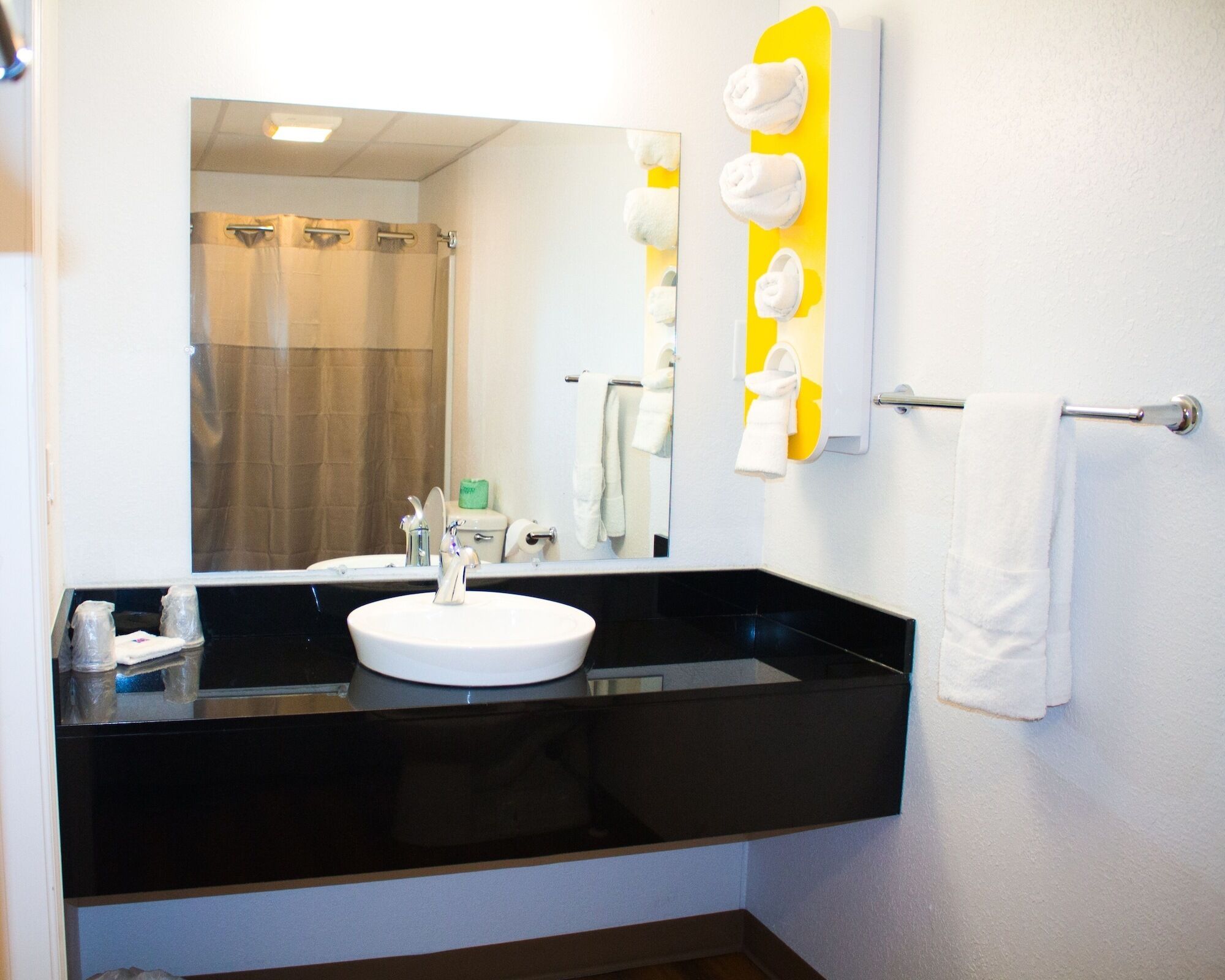 Un baño con lavamanos negro, un espejo y un perchero con toallas.