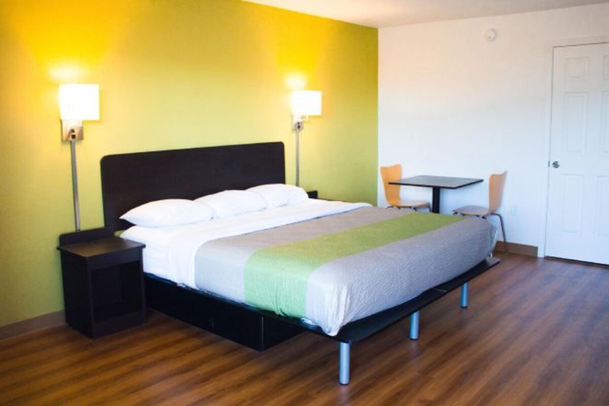 A hotel room with a bed, bedside tables, a chair, a small table, and a door.