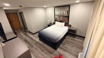 A hotel room with a bed, bedside table, lamp, and a cityscape painting on the wall.