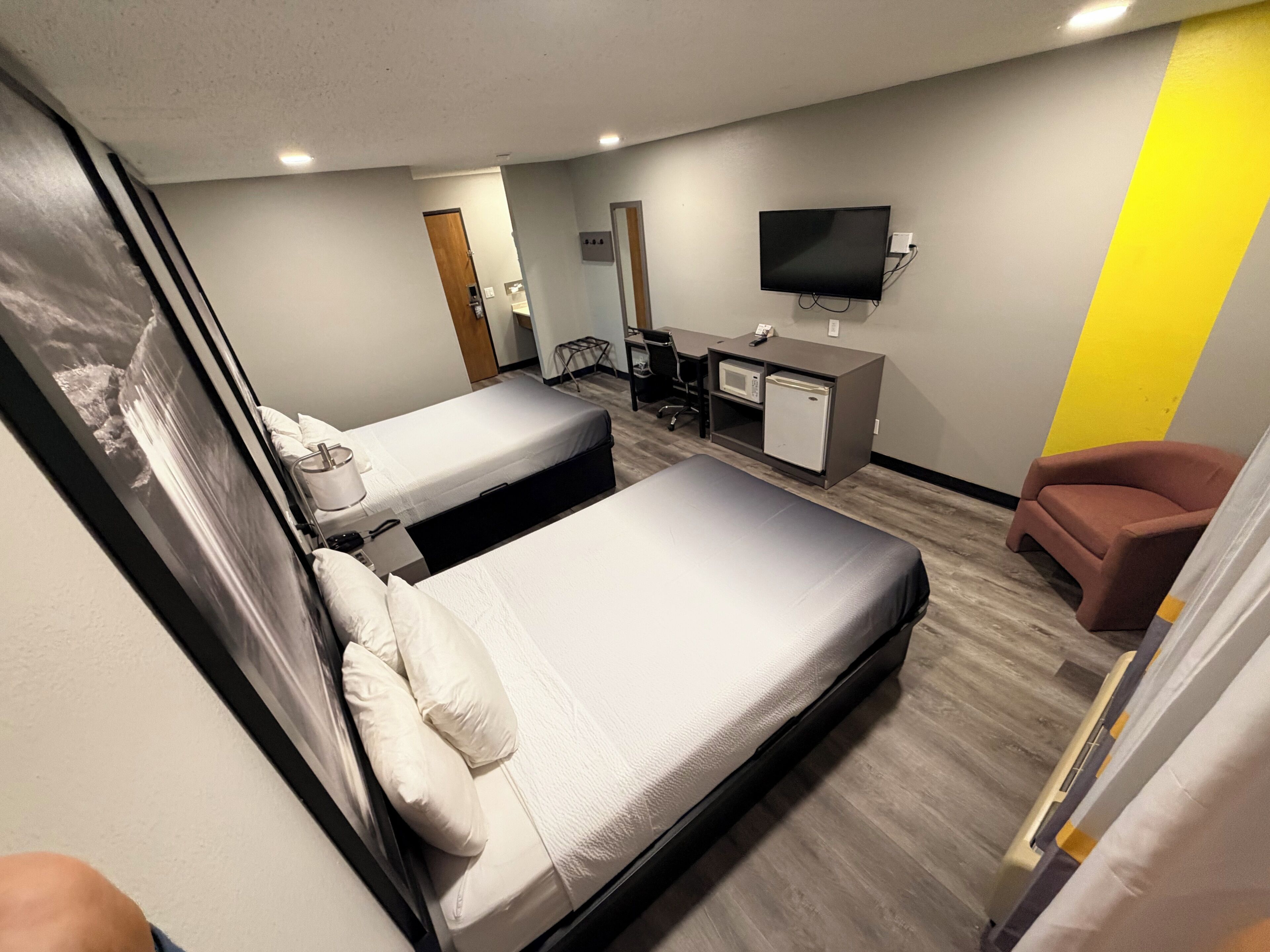 A hotel room with two beds, a desk, a television, and a chair.