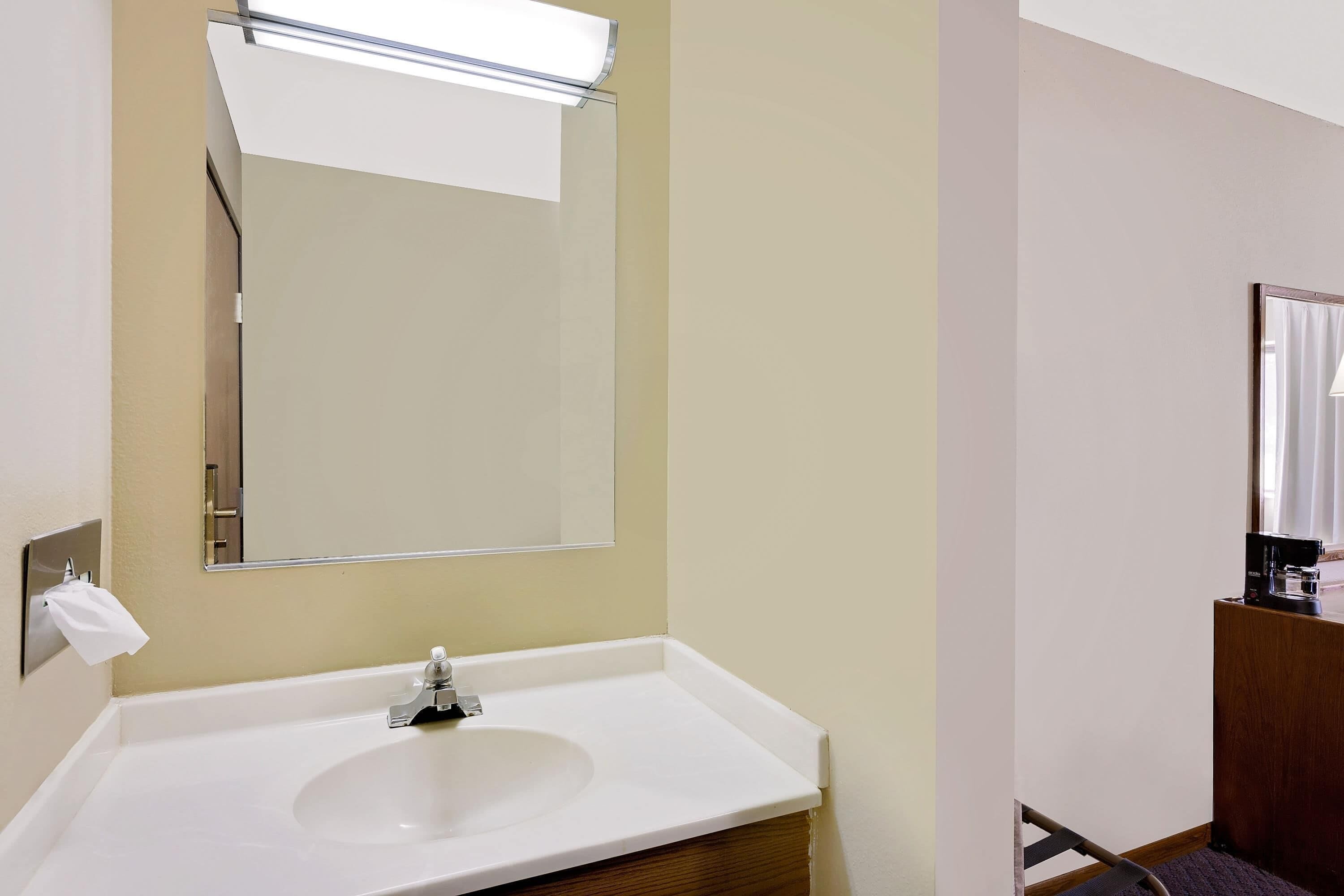 A bathroom with a white sink, a mirror, and a towel dispenser.