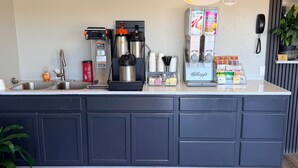Un bar pour le petit-déjeuner équipé d’une machine à café, de bouilloires et d’un réfrigérateur rempli de boissons.