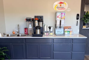 A breakfast bar with a coffee machine, kettles, and a refrigerator stocked with beverages.