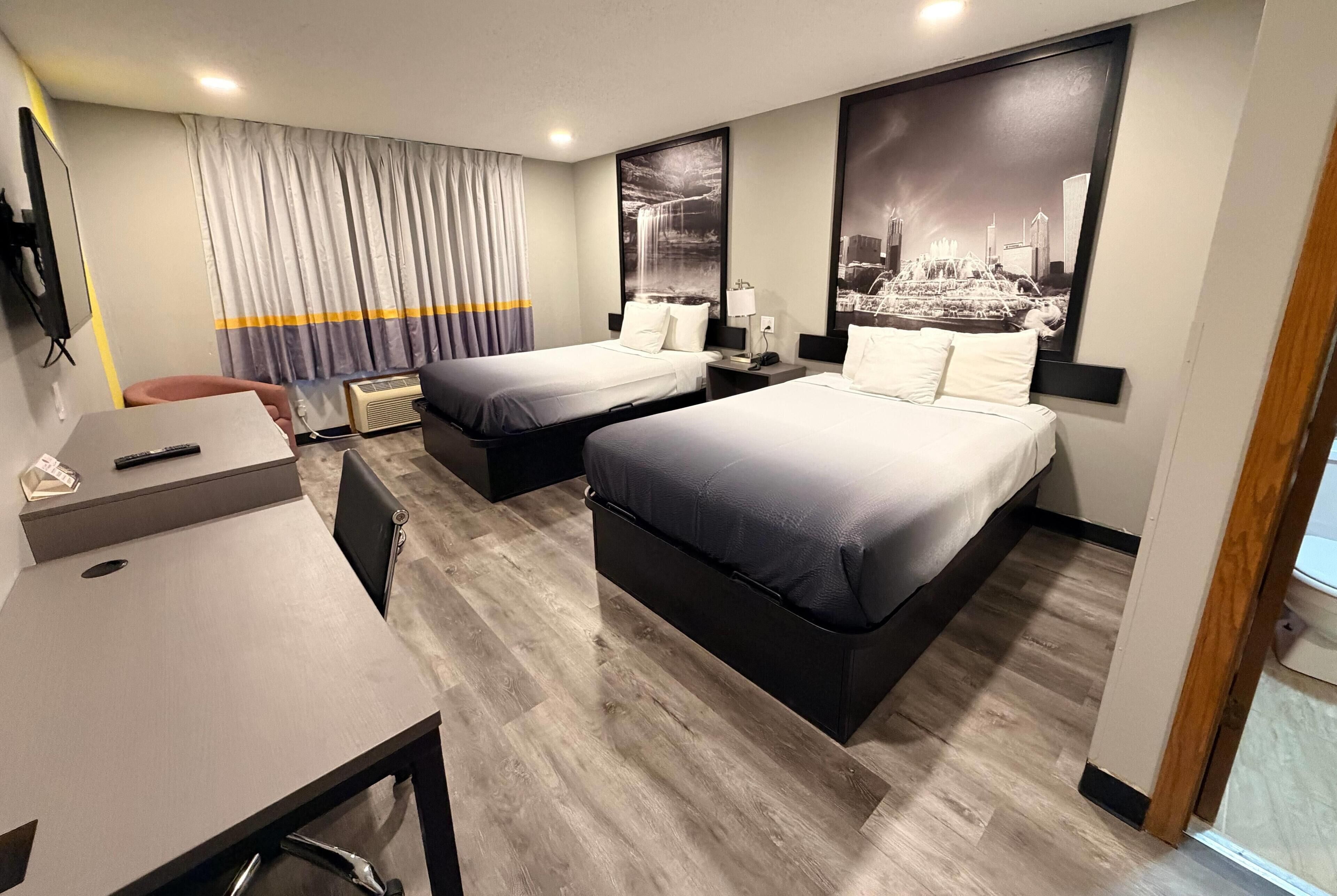 A hotel room with two beds, a desk, a chair, a TV, and a window with curtains.