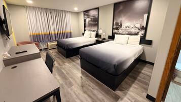 A hotel room with two beds, a desk, a chair, a TV, and a window with curtains.