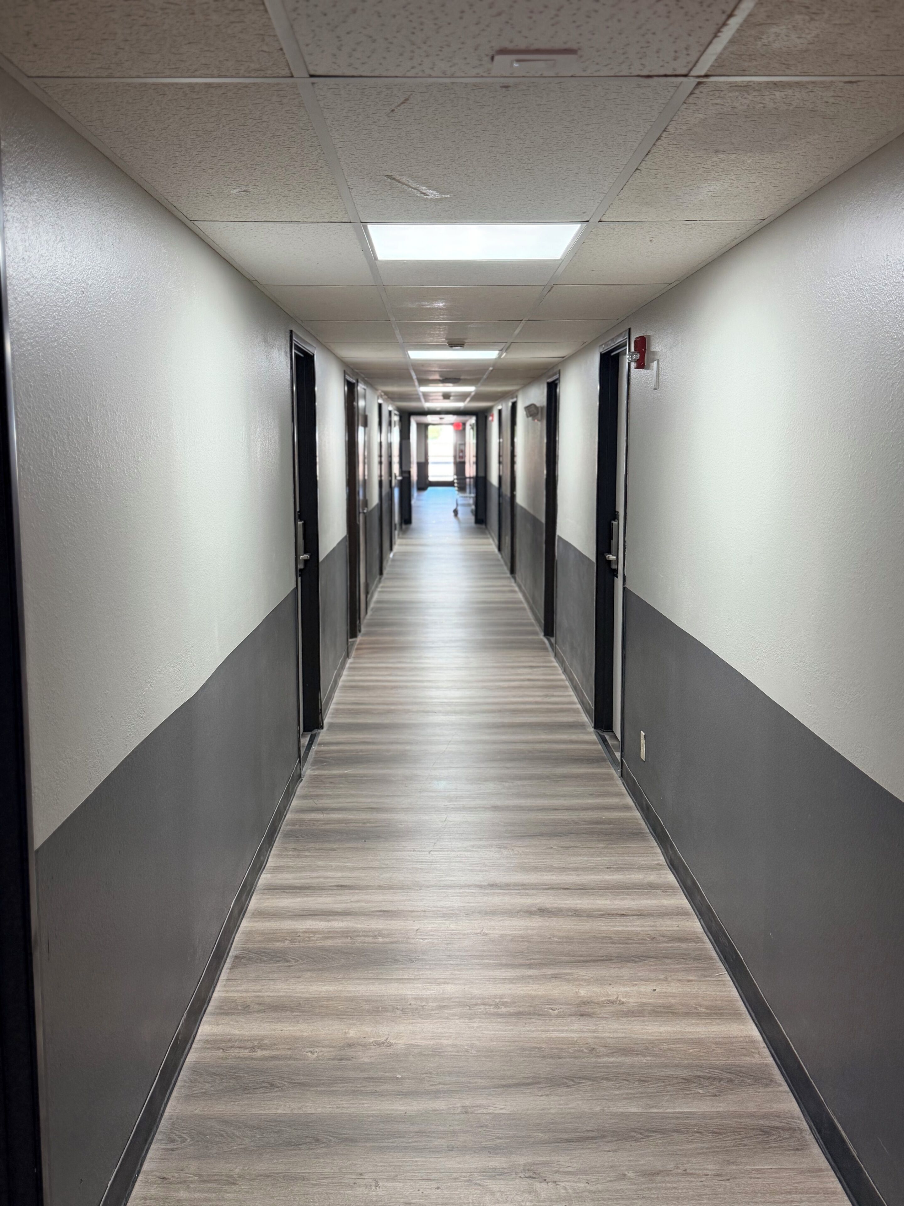 A long, narrow hallway with doors on both sides, a tiled ceiling, and a wooden floor.
