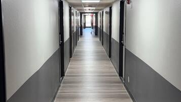 A long, narrow hallway with doors on both sides, a tiled ceiling, and a wooden floor.