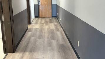 A hallway with a wooden floor, a door at the end, and a light switch on the wall.