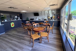 A restaurant interior with a counter, wooden tables and chairs, a TV on the wall, and a view of the outside.