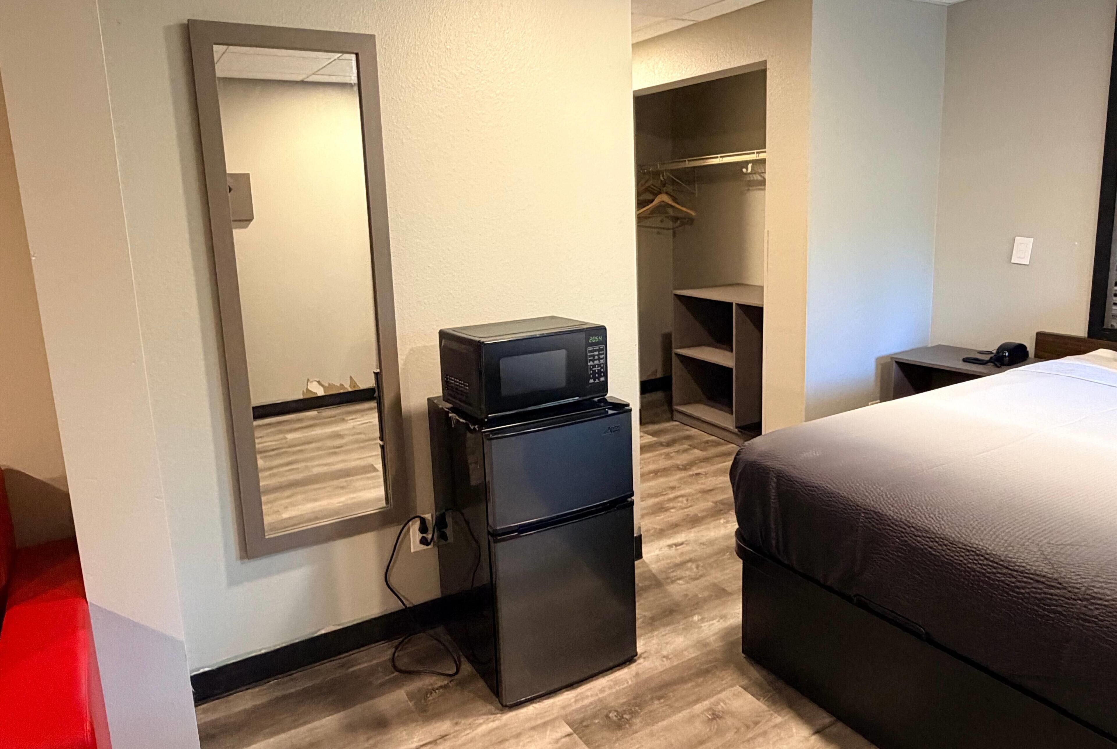 A hotel room with a bed, a refrigerator, a microwave, a closet, and a desk.