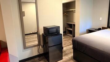 Habitación de hotel con cama, refrigerador, microondas, armario y escritorio.