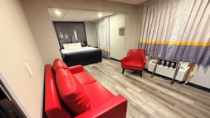 Une chambre d’hôtel moderne avec un canapé rouge, un lit, un fauteuil rouge et une œuvre d’art représentant un paysage urbain accrochée au mur.