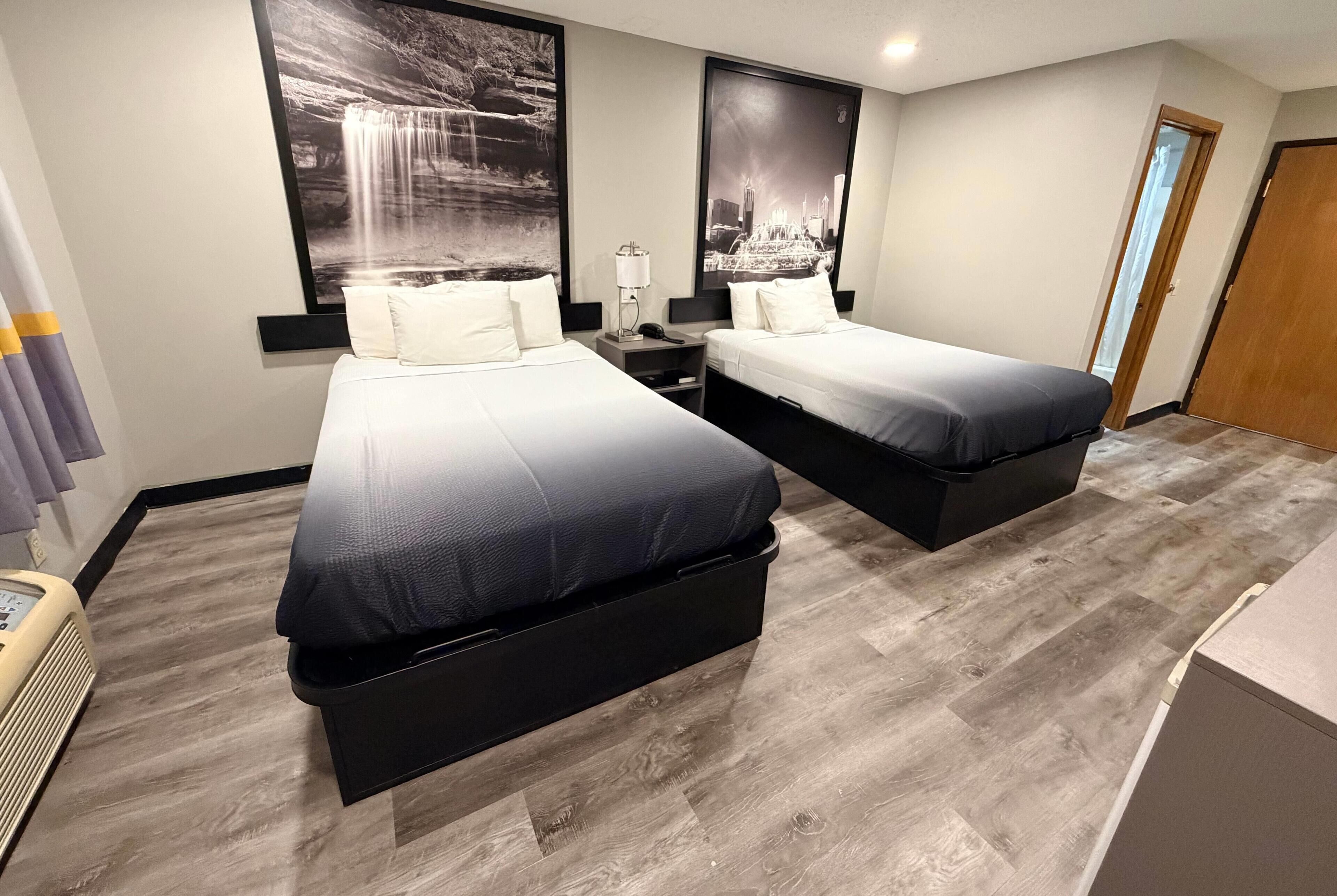 A hotel room with two beds, a nightstand, a lamp, and a large window.