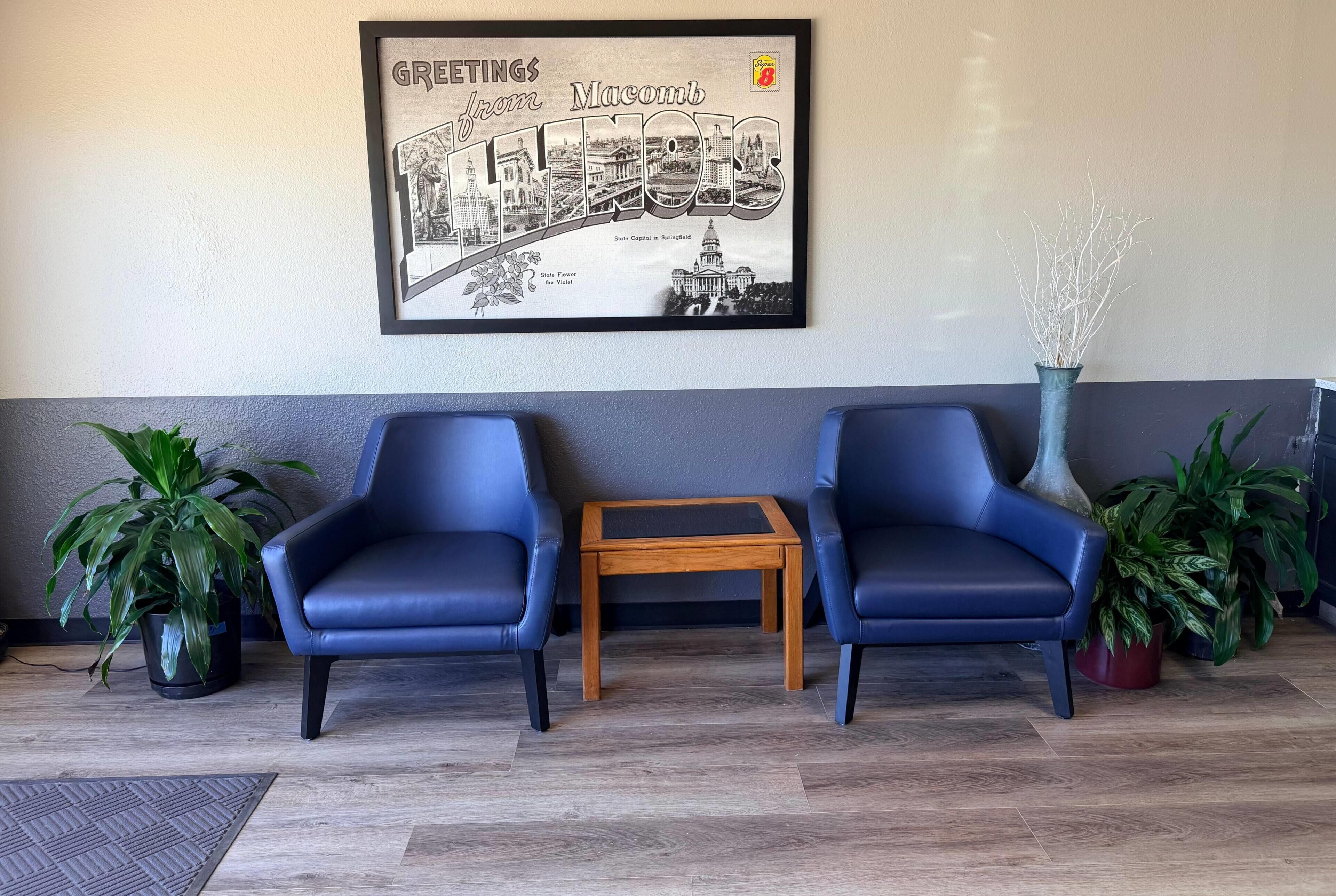 A reception area with two blue chairs, a small wooden table, and a framed welcome sign.
