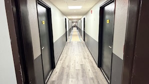 Un long couloir étroit, avec des portes de chaque côté, un plancher en bois et un plafond doté d’un éclairage encastré.