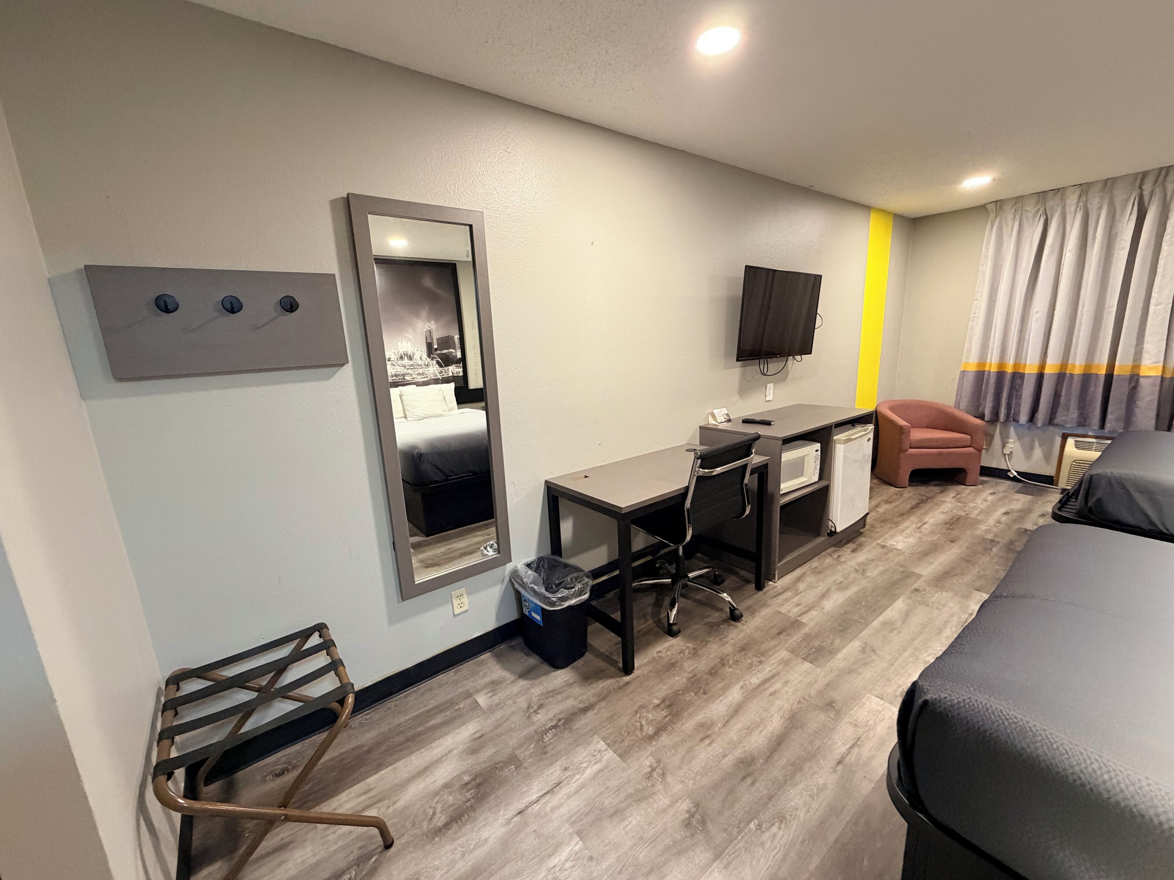 Une chambre d’hôtel équipée d’un lit, d’un bureau, d’une chaise, d’un miroir, d’une télévision et d’une petite kitchenette.