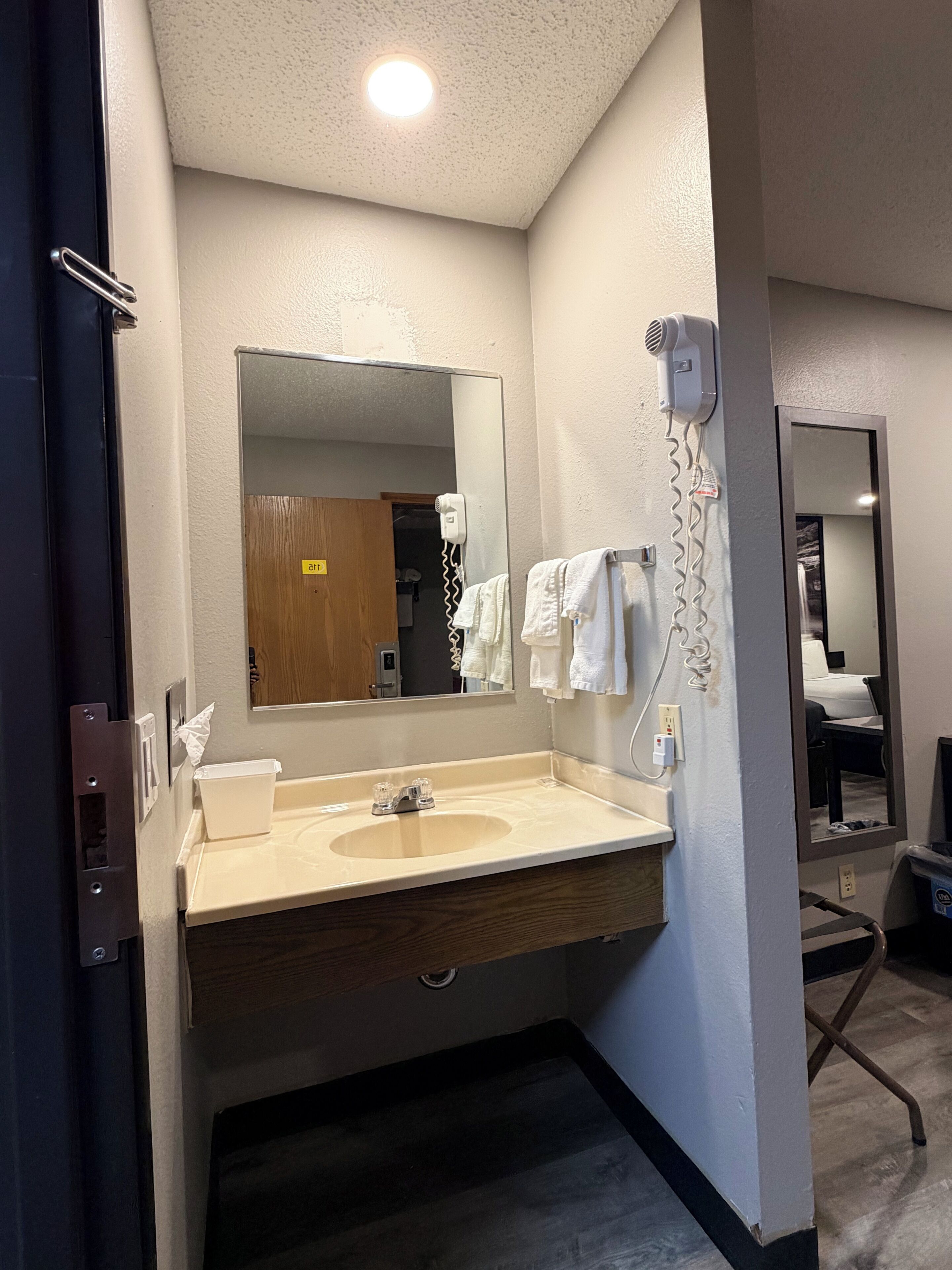 A hotel bathroom with a sink, mirror, towel rack, and hair dryer.
