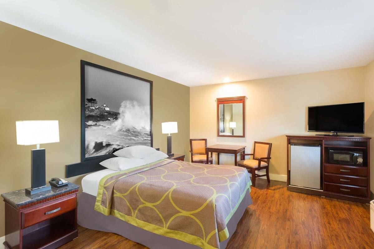 A hotel room with a bed, desk, chair, television, and a refrigerator.