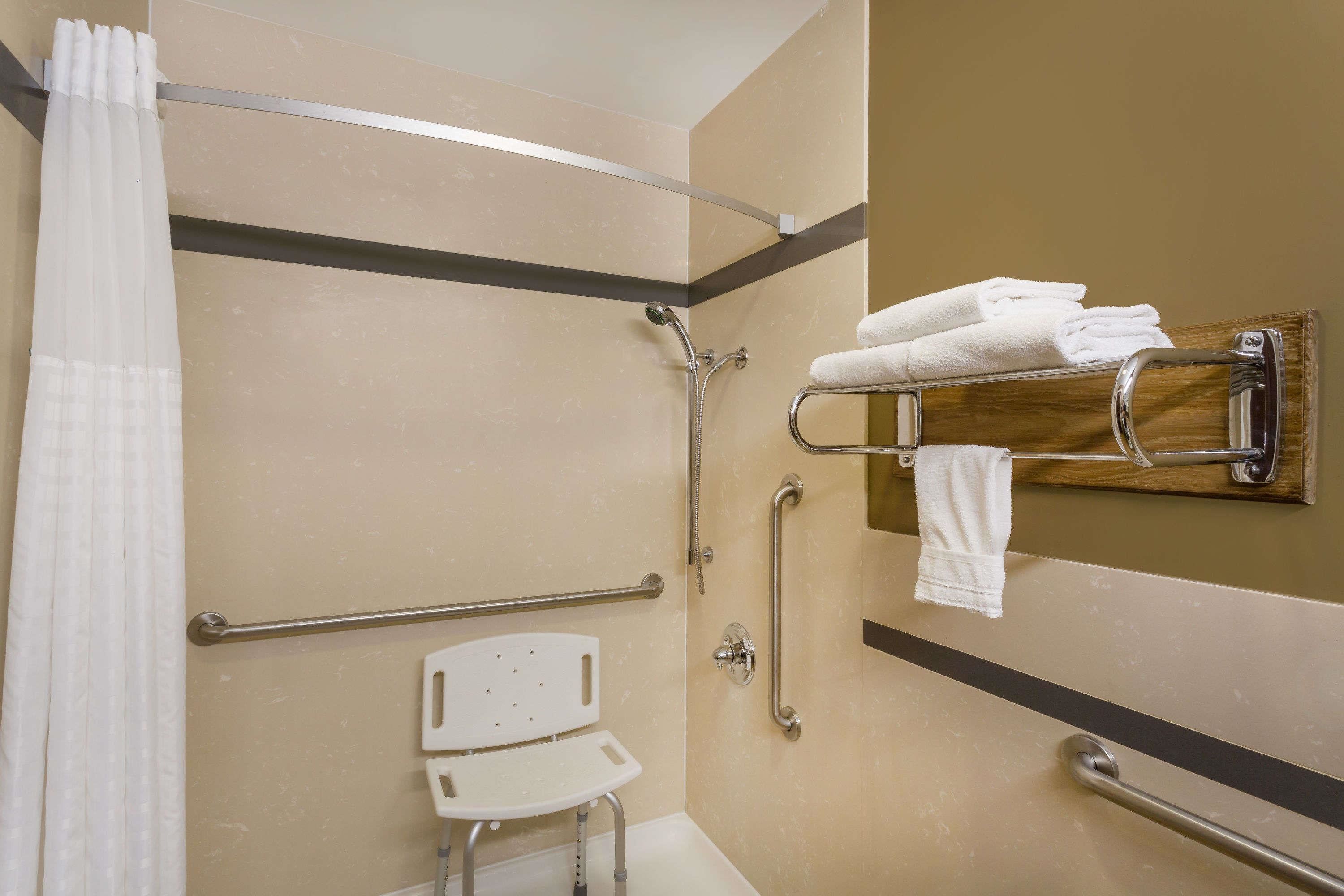 A bathroom with a shower, grab bars, a wheelchair-accessible bench, and a towel rack.