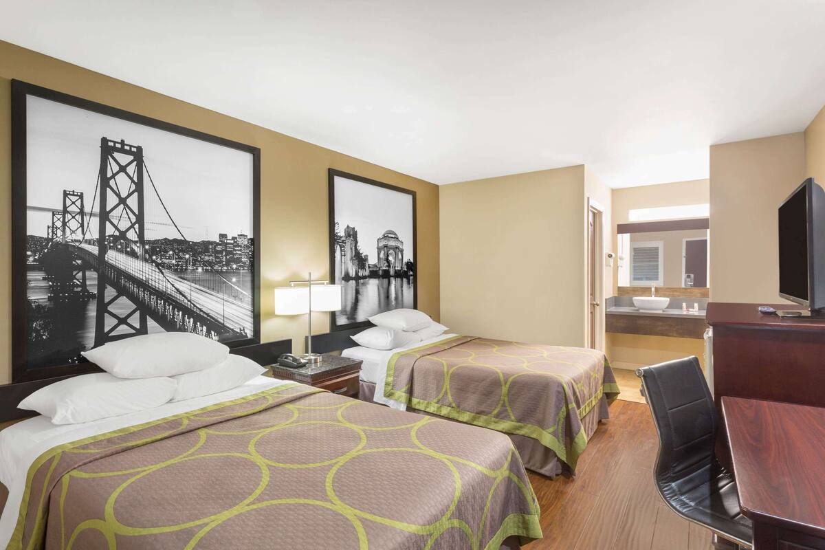 A hotel room with two beds, a desk, a chair, a TV, and two large framed pictures on the wall.
