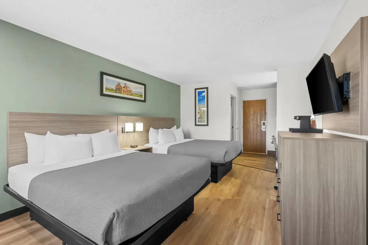 A hotel room with two beds, a television, and a door leading to a hallway.
