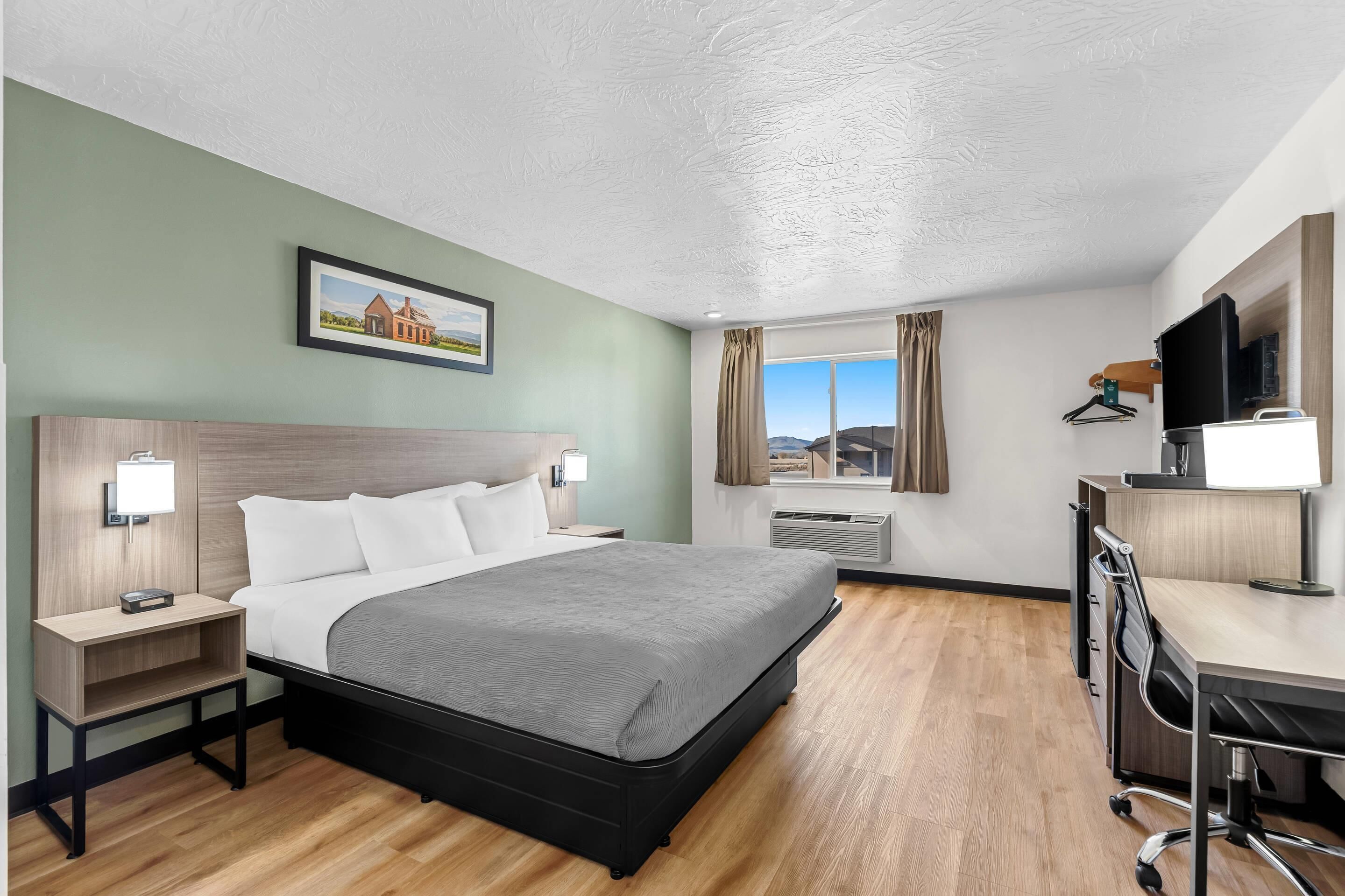 A hotel room with a bed, bedside tables, a desk, a chair, a TV, and a window with curtains.