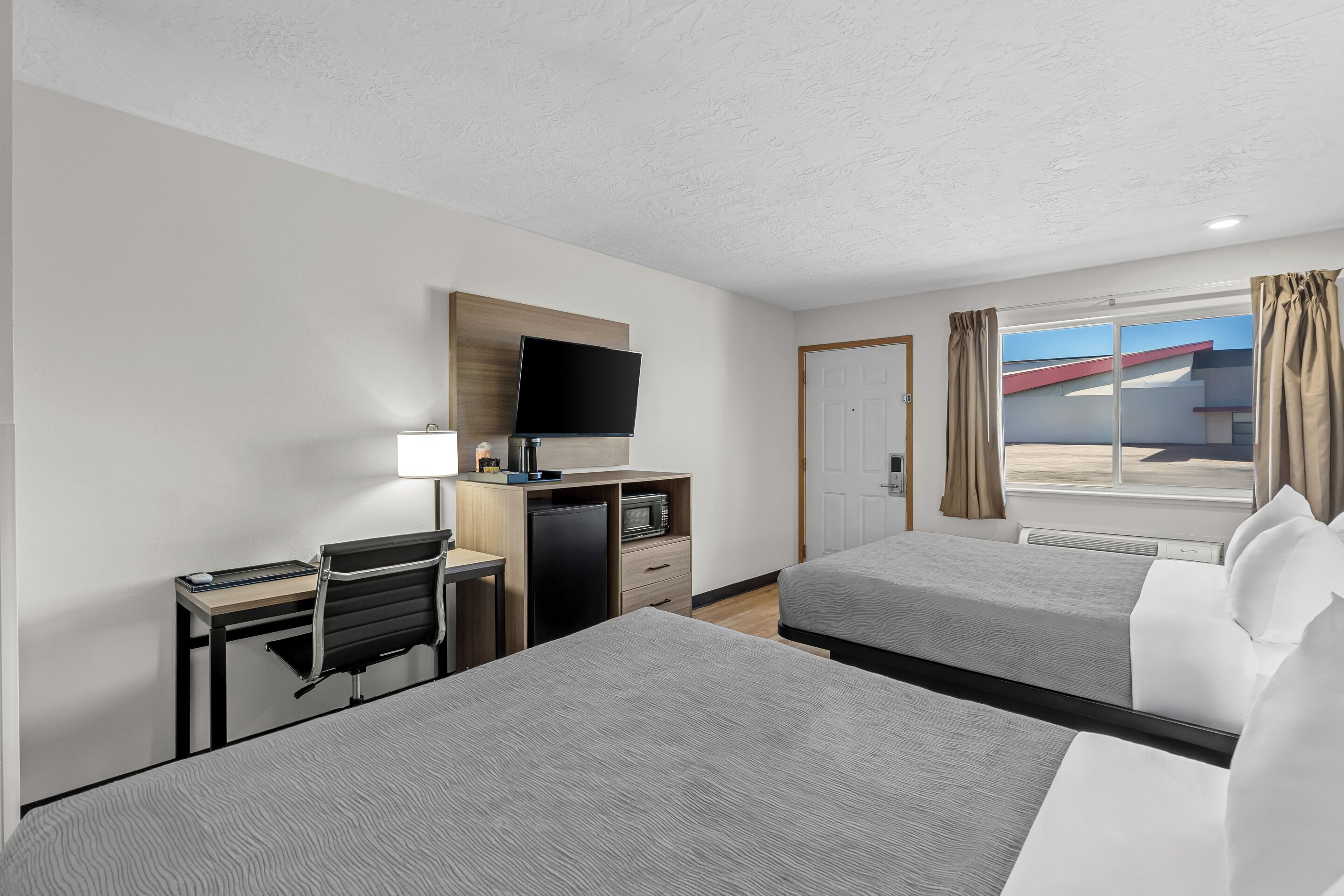 Hotelkamer met twee bedden, een bureau met stoel, een televisie, een minibar en een raam met gordijnen.